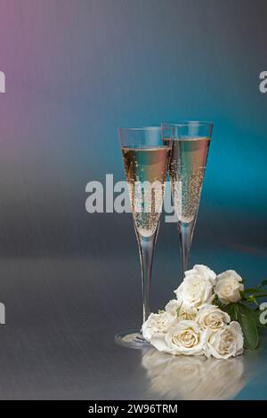 Une nature morte de deux classes de champagne pétillant dans d'élégantes flûtes à champagne avec un bouquet de roses blanches sur un fond Uni Banque D'Images