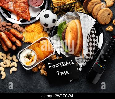 Graisses saturées. L'heure du football. Télécommande TV et collations - chips, pop-corn, biscuits, fromage, sauce, frites, burger, noix. Vue de dessus Banque D'Images