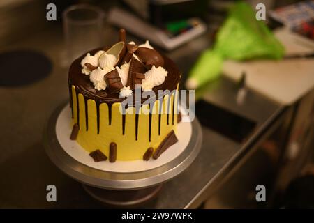 chef pâtissier lisse préparer une sculpture jaune goutte à goutte givré gâteau au chocolat noir superposé orné image haute résolution Banque D'Images