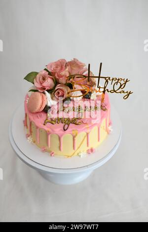 glaçage givré frais égouttant gâteau d'anniversaire rose vanille vraies roses et décoration macaron sur le dessus avec signe doré Banque D'Images