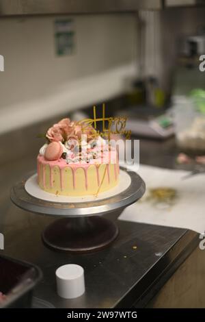 glaçage givré frais égouttant gâteau d'anniversaire rose vanille vraies roses et décoration macaron sur le dessus avec signe doré Banque D'Images
