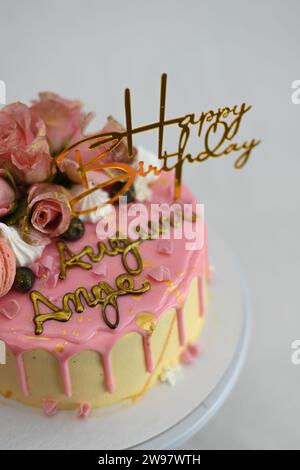 glaçage givré frais égouttant gâteau d'anniversaire rose vanille vraies roses et décoration macaron sur le dessus avec signe doré Banque D'Images