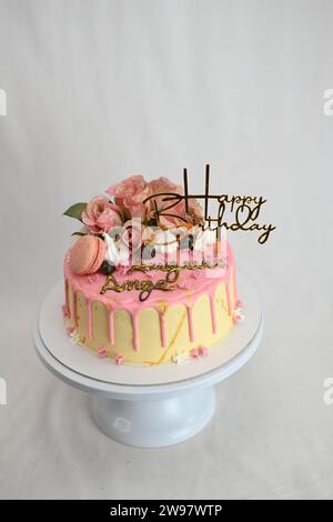 glaçage givré frais égouttant gâteau d'anniversaire rose vanille vraies roses et décoration macaron sur le dessus avec signe doré Banque D'Images
