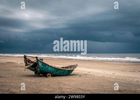 Un vieux bateau de pêche en bois sur une plage sur fond de nuages gris tumultueux Banque D'Images