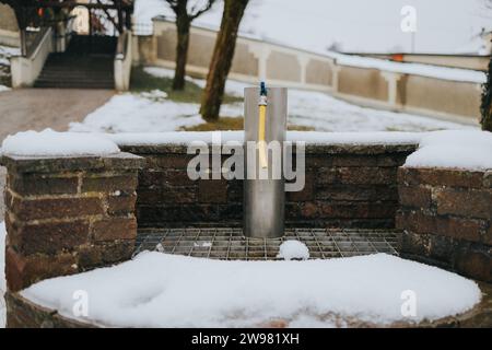 Une scène hivernale mettant en vedette une fontaine d'eau couverte de neige située sur un trottoir devant un mur de briques Banque D'Images