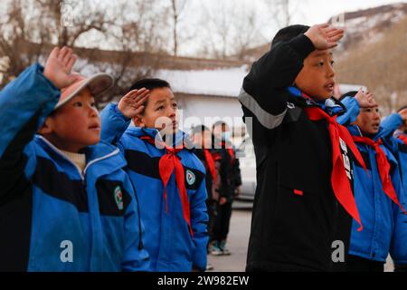 Jishan, province chinoise du Gansu. 25 décembre 2023. Des élèves saluent lors d'une cérémonie de levée de drapeau dans une école primaire du canton de Liugou, dans le comté de Jishan, dans la province du Gansu, au nord-ouest de la Chine, le 25 décembre 2023. Les écoles primaires et secondaires dans les zones de Jishishan touchées par le séisme ont commencé à reprendre les cours lundi après un contrôle de sécurité. Crédit : Fang Xin/Xinhua/Alamy Live News Banque D'Images