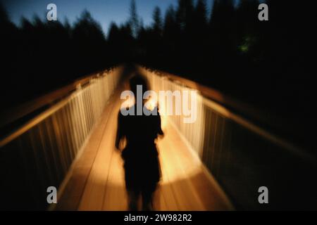 Une femme se profilait contre la lumière de sa lampe de poche en traversant une passerelle. (Flou de mouvement) Banque D'Images