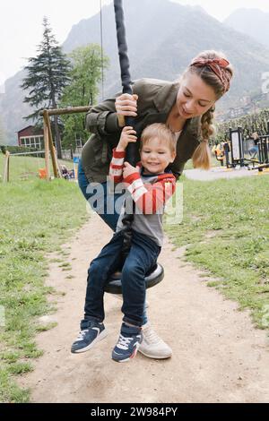 Une femme monte son petit fils sur une tyrolienne pour enfants à l'aire de jeux Banque D'Images