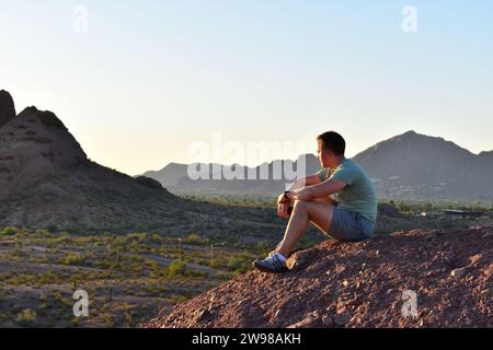 Jeune homme assis au sommet de Hole in the Rock à Phoenix, AZ tout en profitant du coucher du soleil Banque D'Images