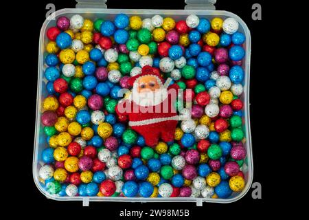Père Noël avec pile de petites boules de thermocol colorées dans une boîte en plastique isolée sur fond noir. Joyeux Noël et nouvel an concept. Banque D'Images