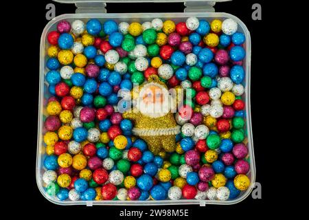 Père Noël avec pile de petites boules de thermocol colorées dans une boîte en plastique isolée sur fond noir. Joyeux Noël et nouvel an concept. Banque D'Images