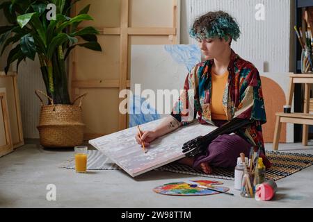 Jeune fille créative avec le bras prothétique esquissant le dessin sur toile en studio Banque D'Images