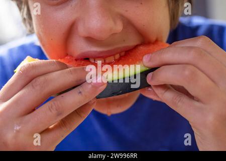 garçon mange un morceau de pastèque rouge avec les deux mains. Journée pastèque Banque D'Images