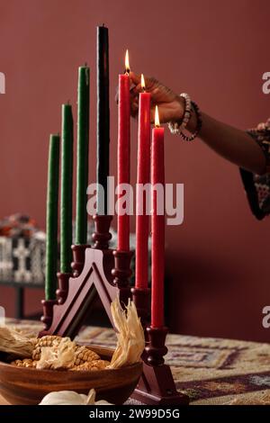 Main de jeune femme afro-américaine méconnaissable allumant des bougies sur le bougeoir tout en se préparant à la célébration de Kwanzaa Banque D'Images