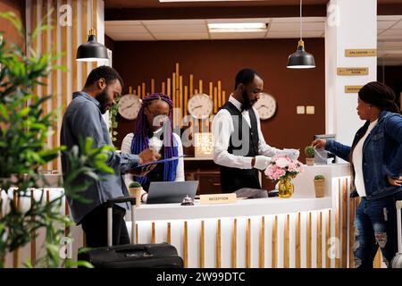 Jeune couple afro-américain remplissant le formulaire d'inscription lors de l'enregistrement à la réception de l'hôtel. Touristes arrivant à la station signant des documents pendant la procédure d'enregistrement, debout à la réception Banque D'Images