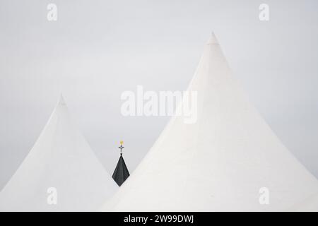 Le sommet d'une flèche d'église avec une bonde dorée montée encadrée par deux toits de tente blancs Banque D'Images