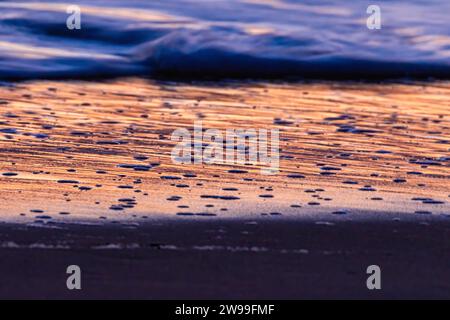 Vue vibrante sur le coucher du soleil des vagues roulantes sur un rivage de plage de sable Banque D'Images
