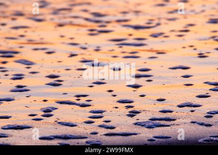 Vue rapprochée à grand angle d'une plage de sable avec des vagues roulantes illuminées par un beau coucher de soleil rose Banque D'Images