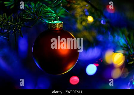 Un ornement de Noël rouge est suspendu à un arbre, éclairé par les lumières vibrantes de la saison des fêtes Banque D'Images