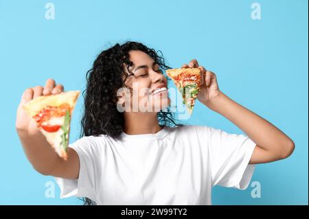 Belle jeune femme afro-américaine heureuse avec des tranches de pizza délicieuse sur fond bleu Banque D'Images