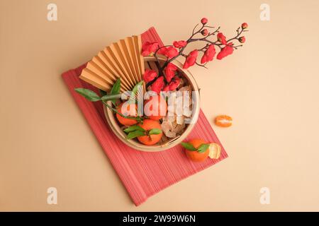 Mandarines, confiture de gingembre, branches de fleurs de pêche et éventail en papier élégamment présentés dans un cuiseur vapeur en bambou sur un fond rose doux. Une toile de sp. Libre Banque D'Images