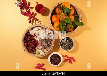 Les paniers vapeur en bambou sont utilisés pour contenir des mandarines, des jujubes, de la confiture, des fruits secs salés et des bonbons gommeux, des graines et des orchidées fraîches sur un fond pastel. Banque D'Images