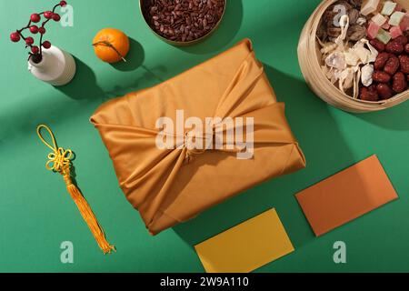 Un tableau cadeau Tet : une boîte cadeau centrale, des plateaux de graines de melon et de confiture, et une enveloppe porte-bonheur sur fond vert, capturée à partir d'un top-vie Banque D'Images