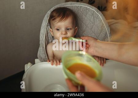 Un petit enfant mange de la purée de légumes. Maman nourrit le bébé. Banque D'Images