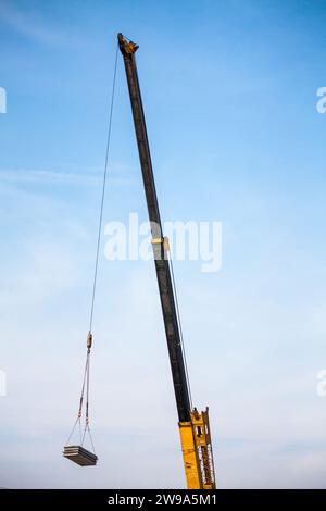 bras télescopiques jaunes de camion de grue de construction mobile soulevant la dalle de béton à la maison de construction au chantier de construction Banque D'Images