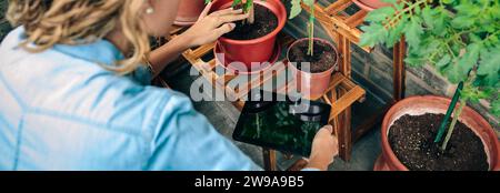Femme utilisant la tablette numérique tout en prenant soin des plantes du jardin urbain sur la terrasse Banque D'Images