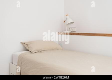Lit simple près de l'étagère murale avec lampe de nuit dans la chambre blanche Banque D'Images