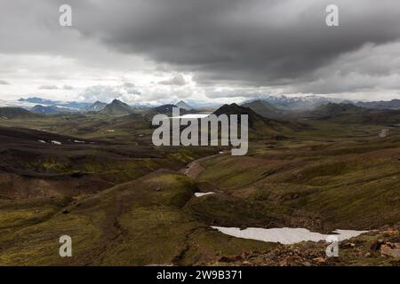 Paysage islandais spectaculaire avec des montagnes vertes couvertes de mousse islandaise épaisse et de taches de neige sur une journée nuageuse grise et moody. Randonnée aventure Islande Banque D'Images