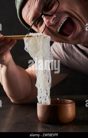 Homme prêt à manger une grande portion de nouilles en verre, une spécialité asiatique, dans un bol en bois Banque D'Images