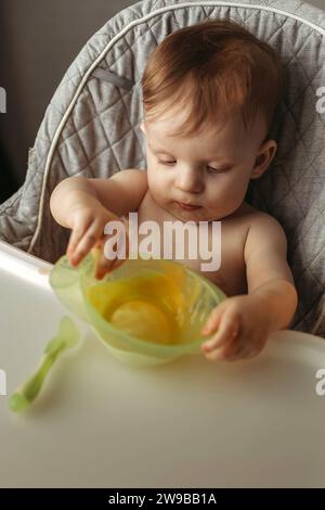 Un petit enfant mange de la purée de légumes. Banque D'Images