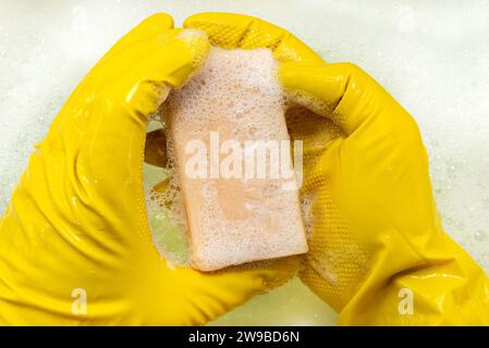 Les mains dans des gants en caoutchouc tiennent une barre de savon dans la mousse de savon. Tâches ménagères Banque D'Images