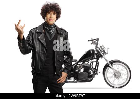 Jeune homme dans une veste en cuir noir faisant signe rock and roll devant une moto isolée sur fond blanc Banque D'Images