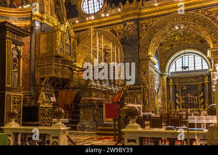 Des chandeliers en argent se dressent devant un pilier de marbre à veines grises dans le presbytère de la co-cathédrale Saint-Jean à La Valette, Malte, avec une vue sur une chaire et une arche sombre menant à une chapelle latérale. L'Ordre de Saint-Jean a fait construire la cathédrale entre 1572 et 1577 ; son intérieur richement doré date essentiellement des années 1660 et suivantes grâce au travail de Mattia Preti. Banque D'Images