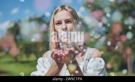 Une fille souffle des confettis en papier multicolores de ses mains. Banque D'Images