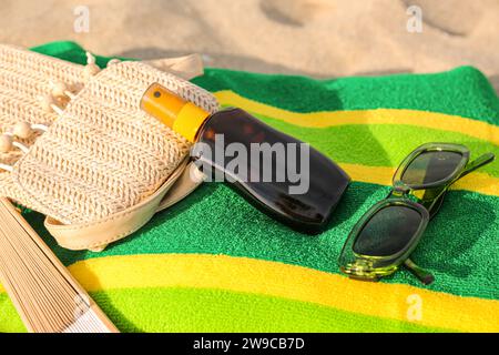 Bouteille de crème solaire avec sac et lunettes de soleil sur fond sablonneux Banque D'Images