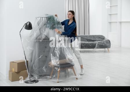 Jeune femme mettant le film plastique loin des meubles à la maison Banque D'Images