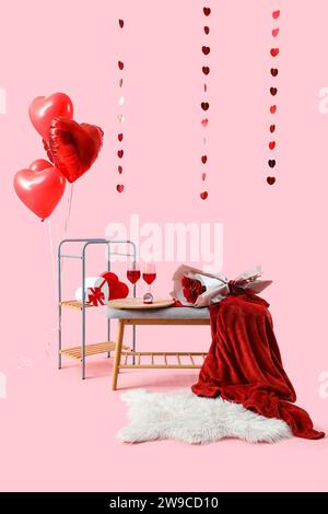 Banc gris avec des verres de vin, des roses et des décorations pour la célébration de la Saint-Valentin sur fond rose Banque D'Images
