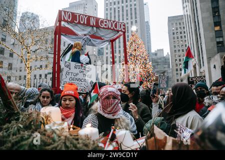 Une foule de manifestants est vue et dans leur arrière-plan se trouve une plate-forme avec l'inscription "No Joy in Genocide" pendant la manifestation. Le jour de Noël, après avoir construit une scène de nativité avec des décombres, du faux sang et des poupées inusées, des centaines de partisans de la Palestine à New York descendent dans la rue pour appeler à un cessez-le-feu immédiat à Gaza. La manifestation est organisée en solidarité avec les églises chrétiennes de Bethléem, qui ont annulé les célébrations de Noël en raison du bombardement continu de Gaza. (Photo Olga Fedorova/SOPA Images/Sipa USA) Banque D'Images