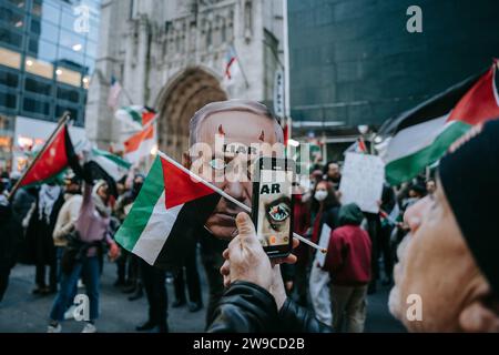 Un manifestant pro-palestinien prend une photo de l'un des manifestants portant un masque représentant le Premier ministre israélien Netanyahu pendant la manifestation. Le jour de Noël, après avoir construit une scène de nativité avec des décombres, du faux sang et des poupées inusées, des centaines de partisans de la Palestine à New York descendent dans la rue pour appeler à un cessez-le-feu immédiat à Gaza. La manifestation est organisée en solidarité avec les églises chrétiennes de Bethléem, qui ont annulé les célébrations de Noël en raison du bombardement continu de Gaza. Banque D'Images