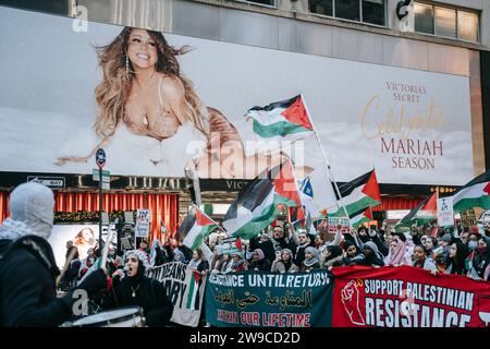 New York, États-Unis. 25 décembre 2023. Les manifestants brandissent des drapeaux palestiniens, des pancartes et des banderoles pendant la manifestation. Le jour de Noël, après avoir construit une scène de nativité avec des décombres, du faux sang et des poupées inusées, des centaines de partisans de la Palestine à New York descendent dans la rue pour appeler à un cessez-le-feu immédiat à Gaza. La manifestation est organisée en solidarité avec les églises chrétiennes de Bethléem, qui ont annulé les célébrations de Noël en raison du bombardement continu de Gaza. Crédit : SOPA Images Limited/Alamy Live News Banque D'Images