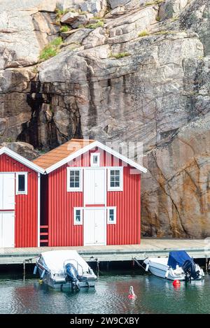 Entrepôt avec façade en bois rouge devant des rochers de granit sur la promenade du port de Smögen dans l'archipel de la côte ouest suédoise Banque D'Images