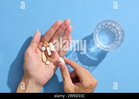 Gros plan de la main d'une femme tenant plusieurs pilules avec un verre d'eau. Prenant des médicaments pour soulager les maux de tête, la gestion de la douleur, l'eau potable de t Banque D'Images