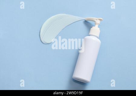 Une bouteille de lotion à pompe non étiquetée, une traînée de crème à texture dense sur fond bleu. La buse de pompe est une conception commune souvent utilisée dans le cosmet Banque D'Images