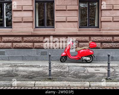 Scooter rouge sur le trottoir devant une maison en grès. Banque D'Images