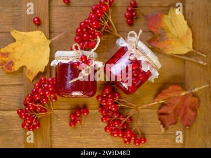 confiture de viburnum. Baies juteuses rouges d'un viburnum avec du sucre dans un bocal en verre sur un fond en bois foncé. Pour faire de la confiture, du thé. Plante médicinale. Banque D'Images