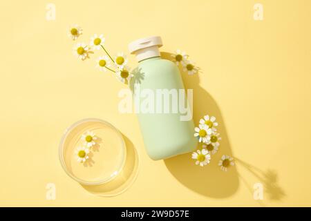 Maquette bouteille sans étiquette avec des fleurs de chamomilla fraîches et boîte de Pétri décorée sur fond jaune. Photo publicitaire pour cosmétiques avec ingrédient f Banque D'Images